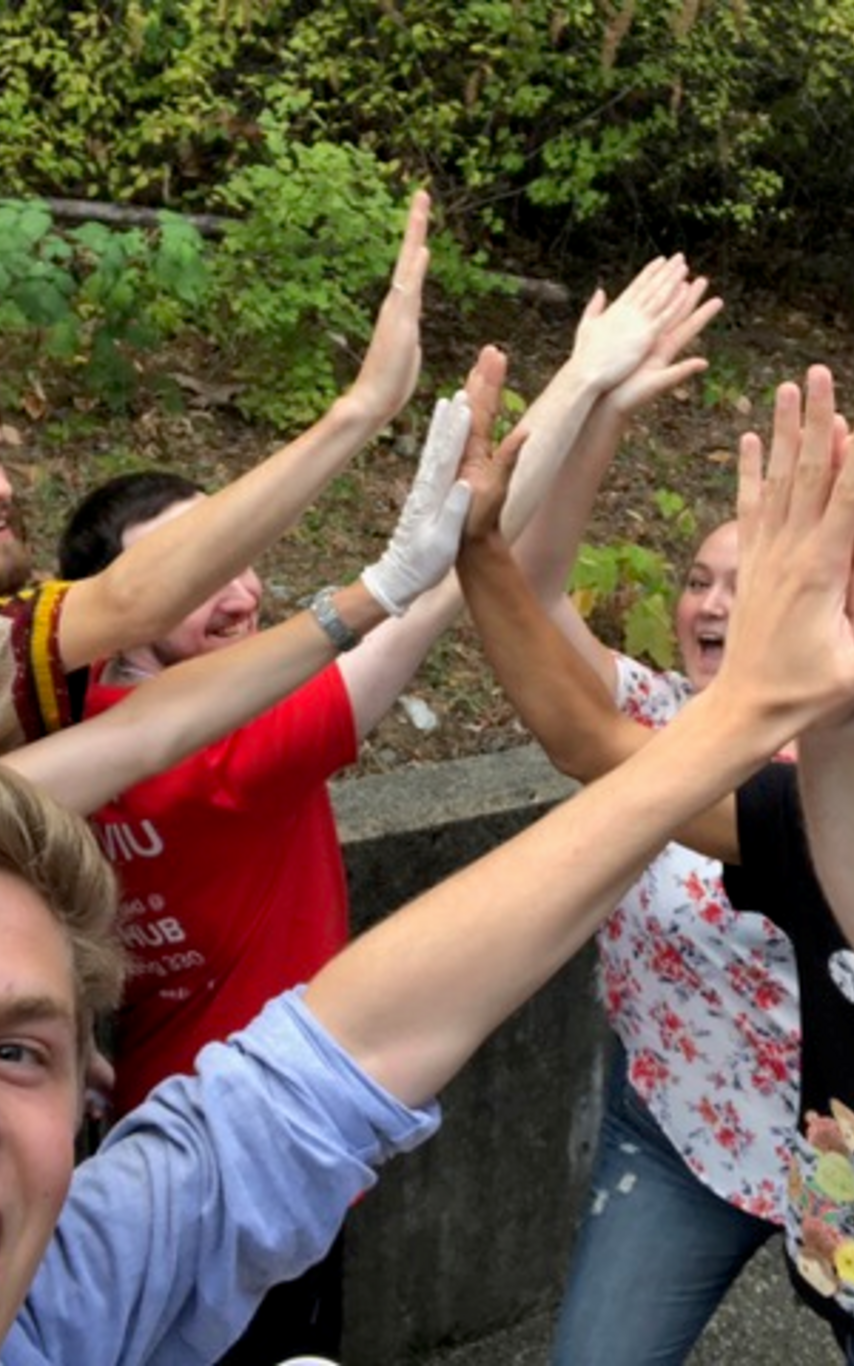 A group of students outside hi-fiving each other with big smiles 